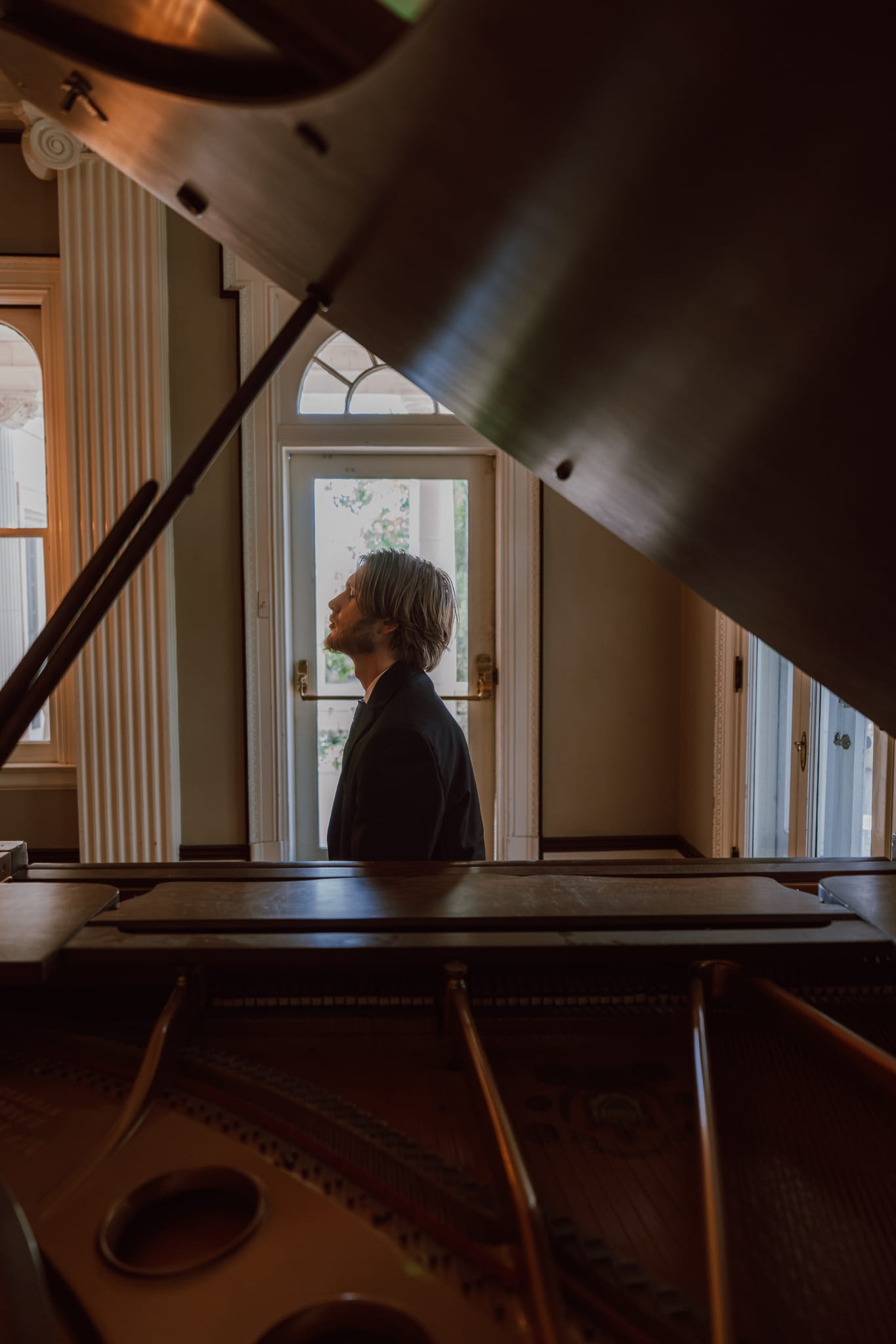 Abe seen through the open lid of a grand piano, framed by its strings and soundboard
