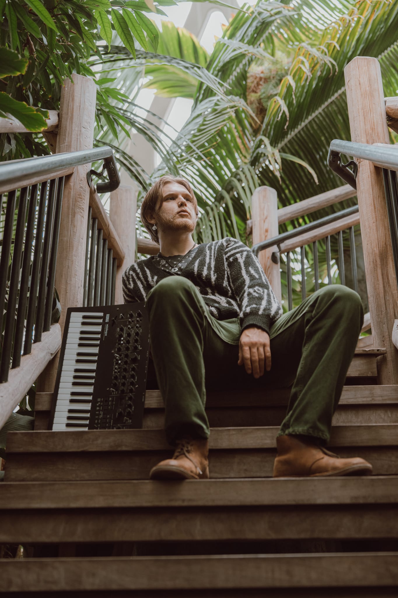 Abe sitting on wooden conservatory stairs among palm fronds, a keyboard leaning against the railing