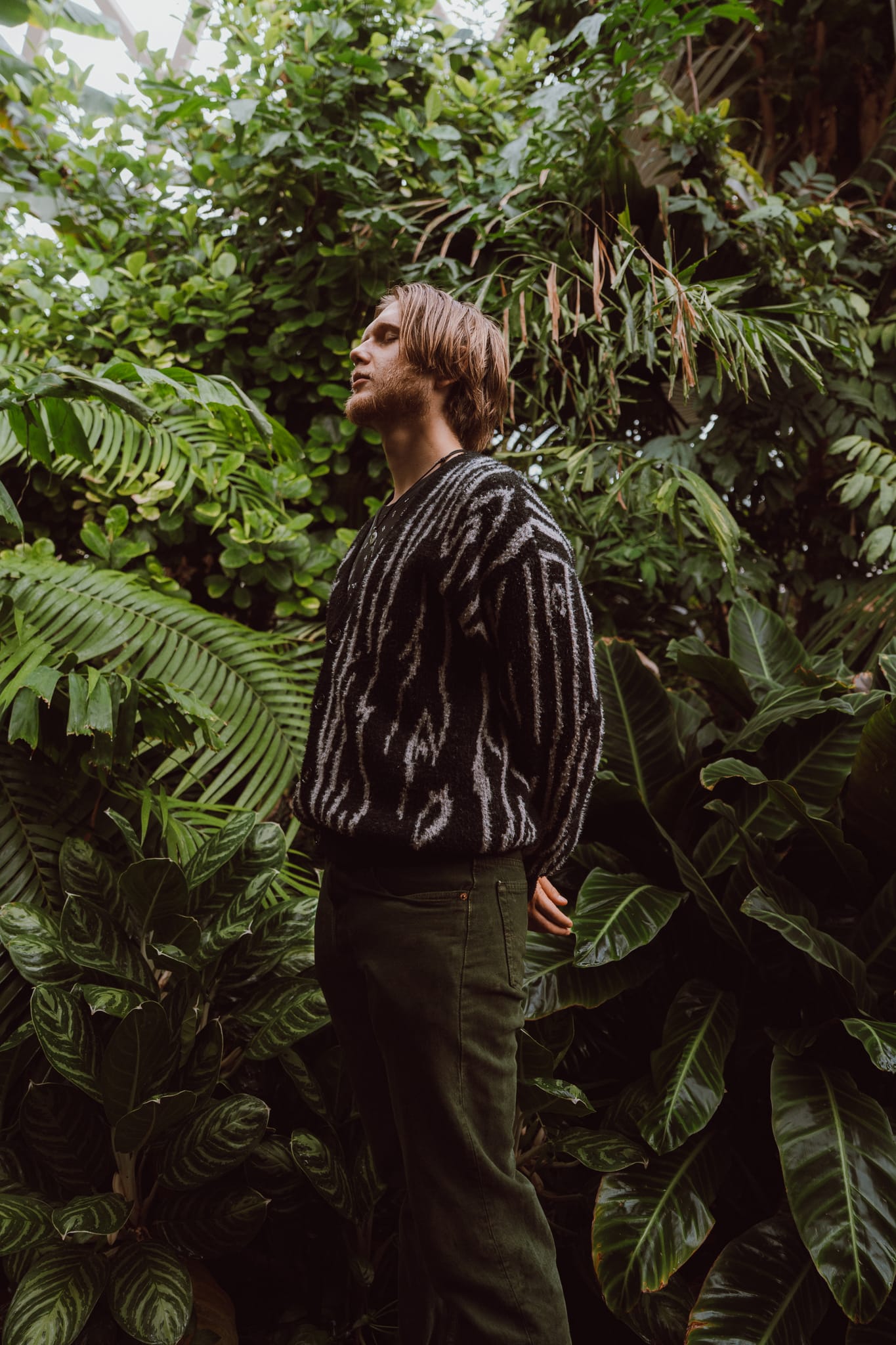 Abe in a patterned sweater standing among dense tropical foliage