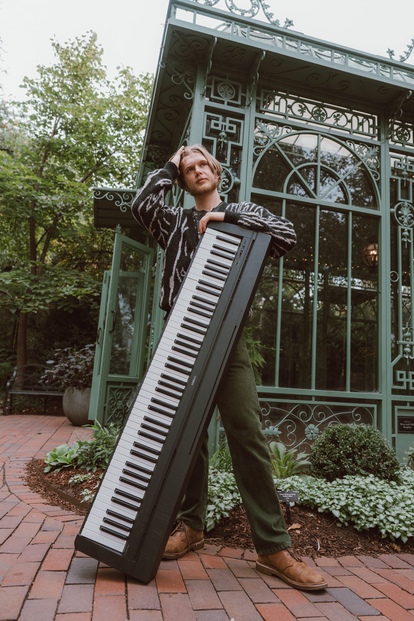 Abe holding a digital keyboard diagonally across his body in front of an ornate green greenhouse
